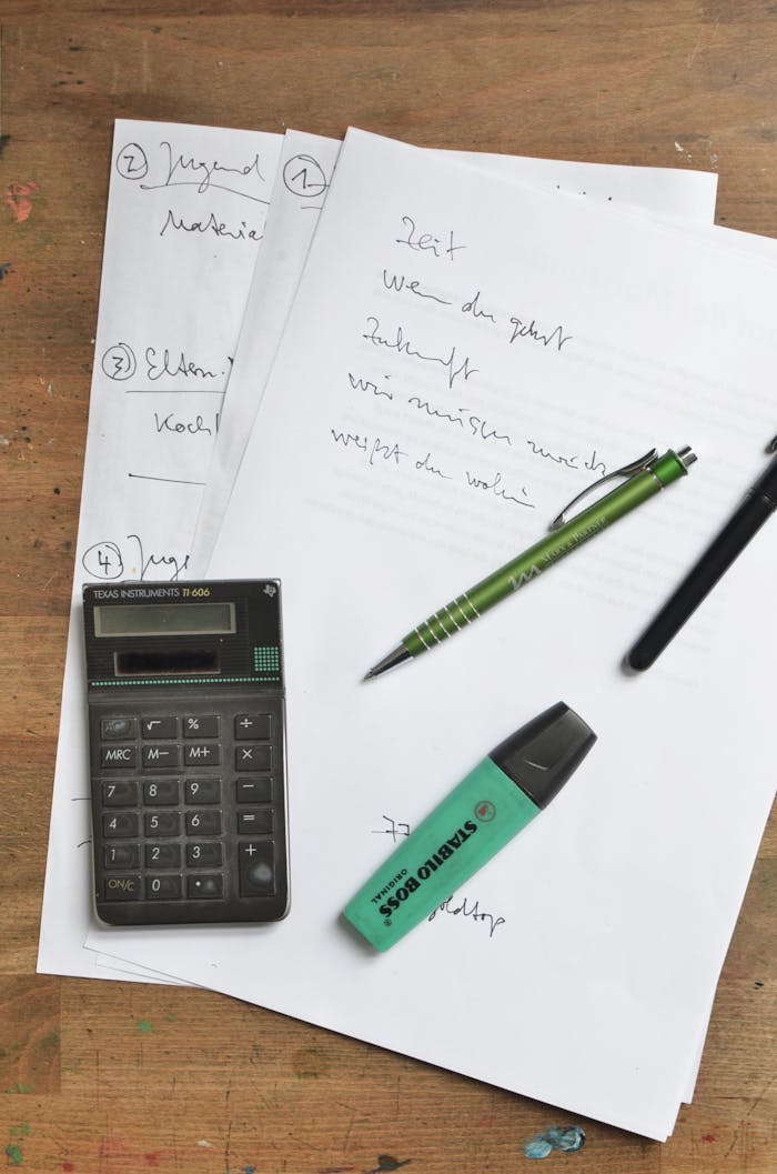 Top view of pen and highlighter near calculator placed on paper sheets with handwritten plan on shabby wooden table
